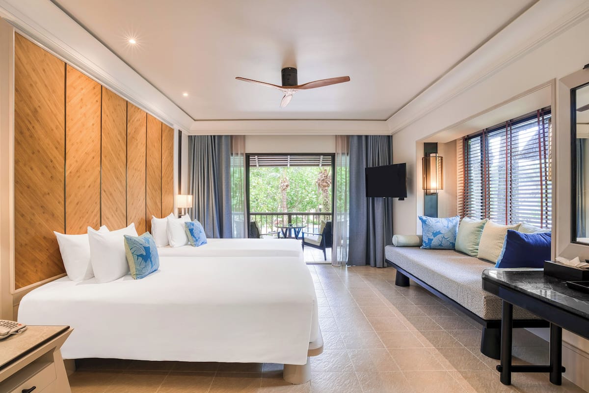A hotel room with a large bed, a desk, and a seating area with a view of greenery outside.