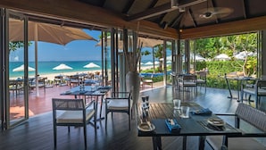 An outdoor dining area with tables and chairs, overlooking a beach with umbrellas. - Layana Resort and Spa - Adult Only (Ko Lanta)
