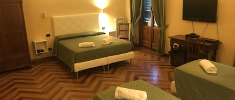 A hotel room with two beds, a desk, a chair, a TV, and a wooden wardrobe.