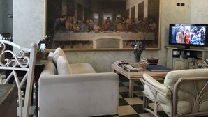 A living room with a large painting of 'The Last Supper' on the wall, a television, and a coffee table with books and a vase of flowers. - Hotel Giglio (Florence)