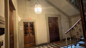 A checkered floor, a staircase with ornate railings, and a hanging light fixture in a hallway. - Hotel Giglio (Florence)