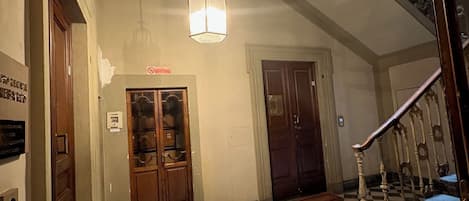 A checkered floor, a staircase with ornate railings, and a hanging light fixture in a hallway.