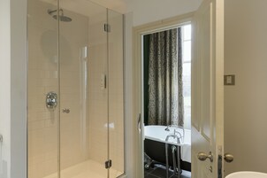 A modern bathroom with a glass-enclosed shower, a white bathtub, and a window with curtains.