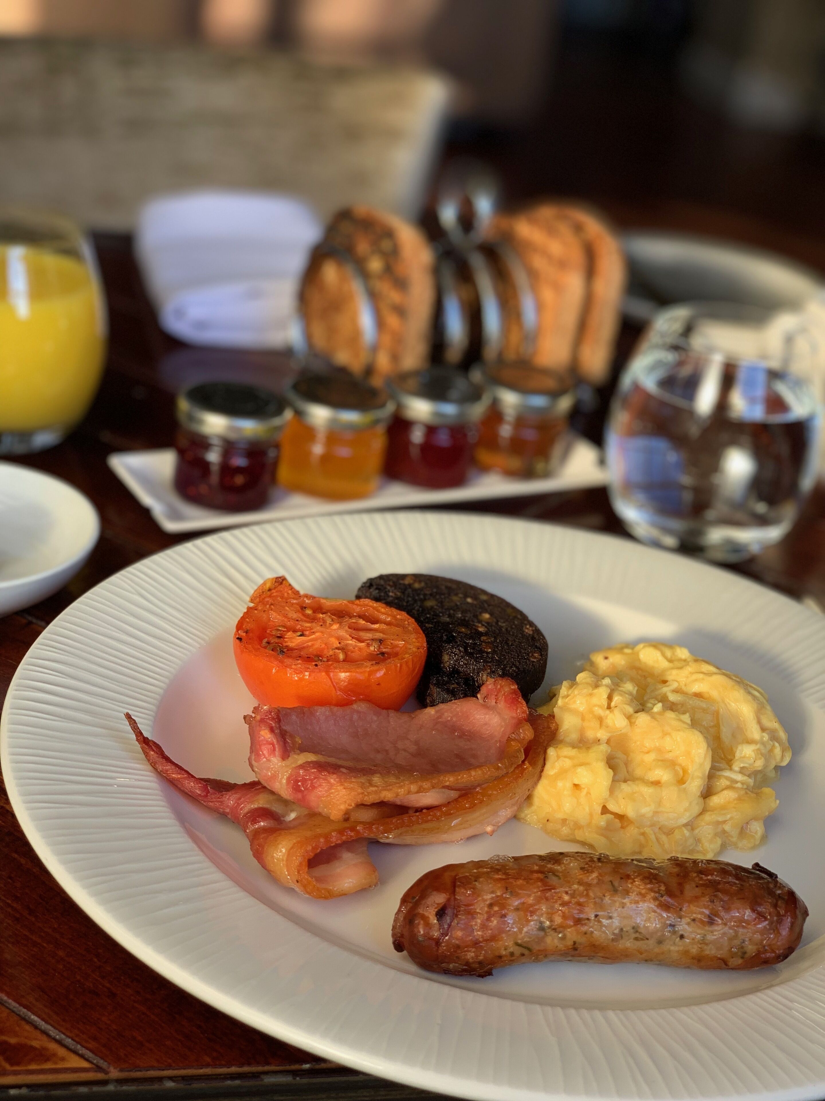 Un plato de desayuno con huevos, tocino, salchicha, tomate y tostadas.