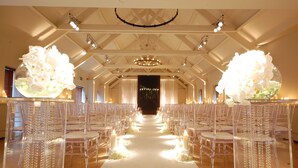 A wedding aisle with clear chairs, white flowers, and candles.
