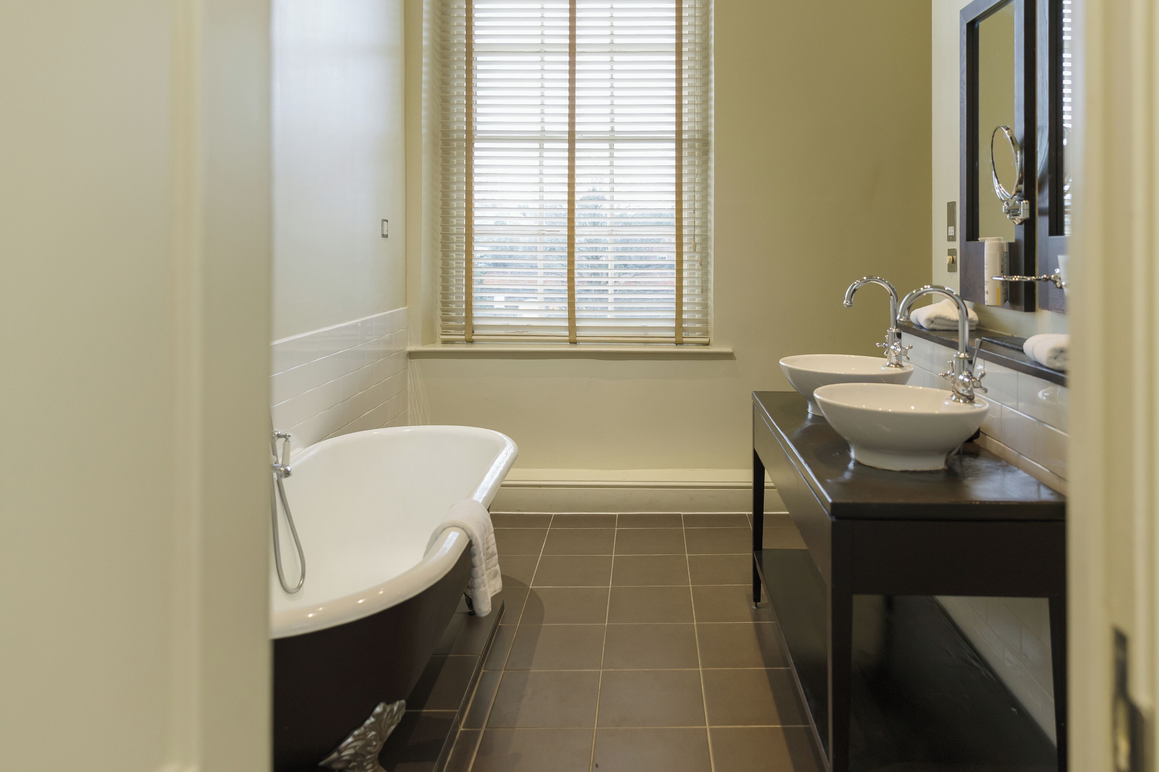 A modern bathroom with a freestanding bathtub, two sinks, and a large mirror.