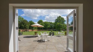 An open door leading to a patio with stone flooring, outdoor furniture, and a lawn.