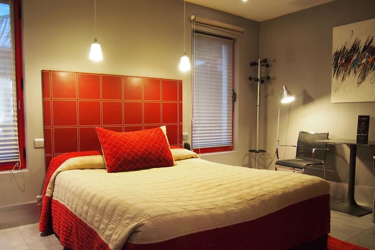 A bedroom with a large bed, a red headboard, a desk with a chair, and a floor lamp.