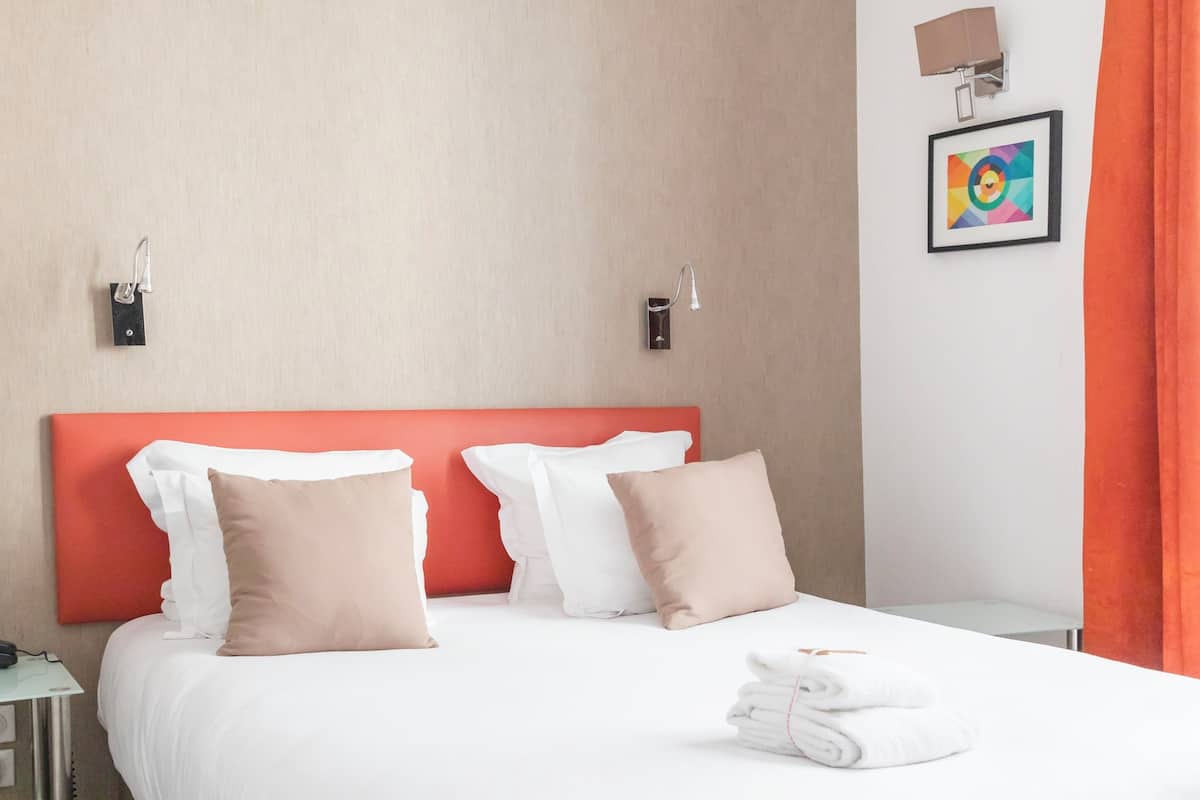 A hotel room with a bed, pillows, a nightstand, a lamp, and a framed picture on the wall.
