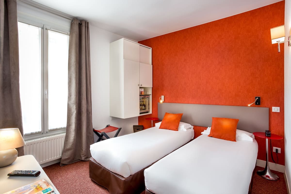 A hotel room with two beds, a desk with a lamp, a small table, and a wardrobe.