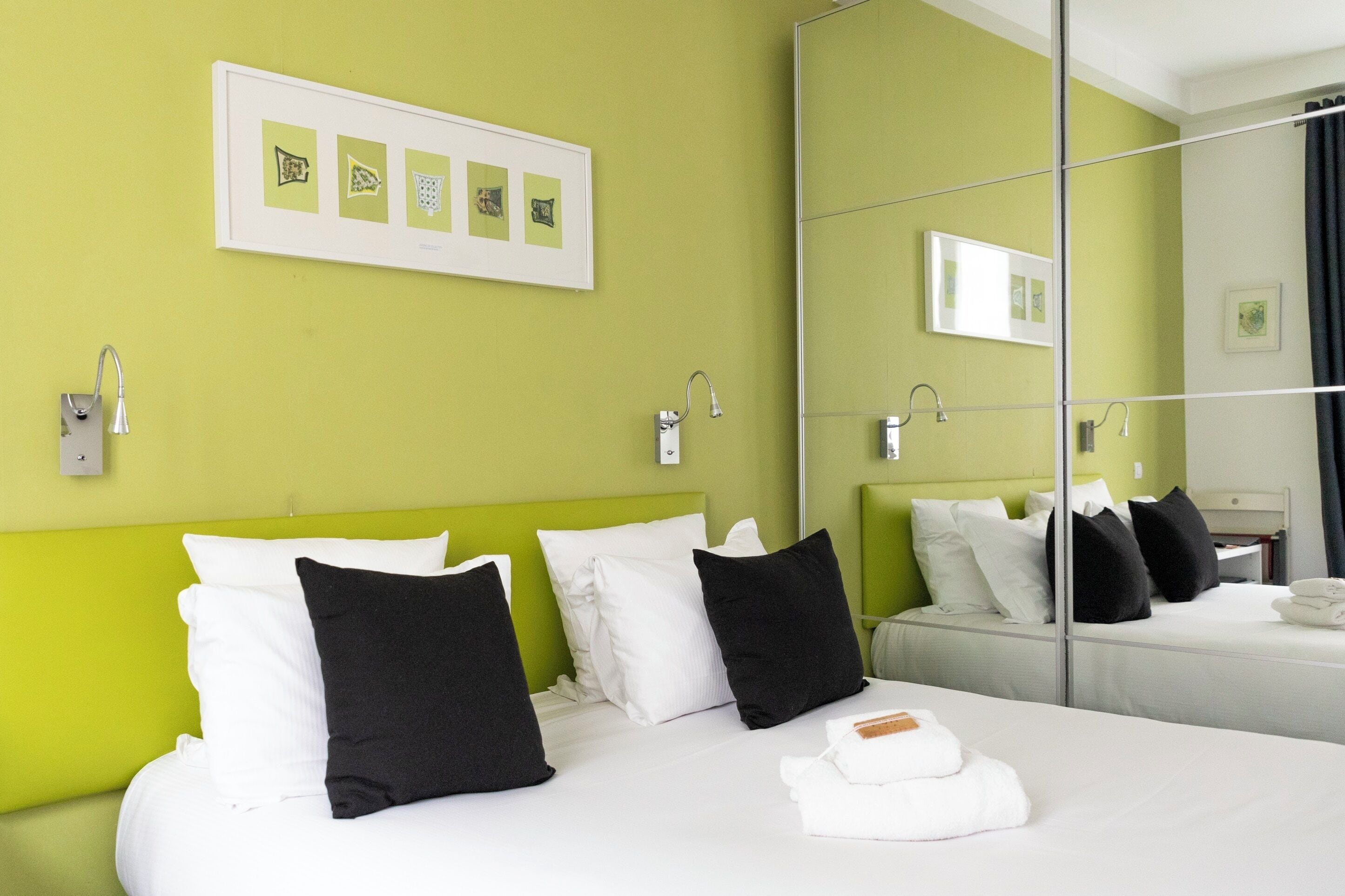 A hotel room with two beds, green walls, white bedding, black pillows, a framed picture, and a large mirror.