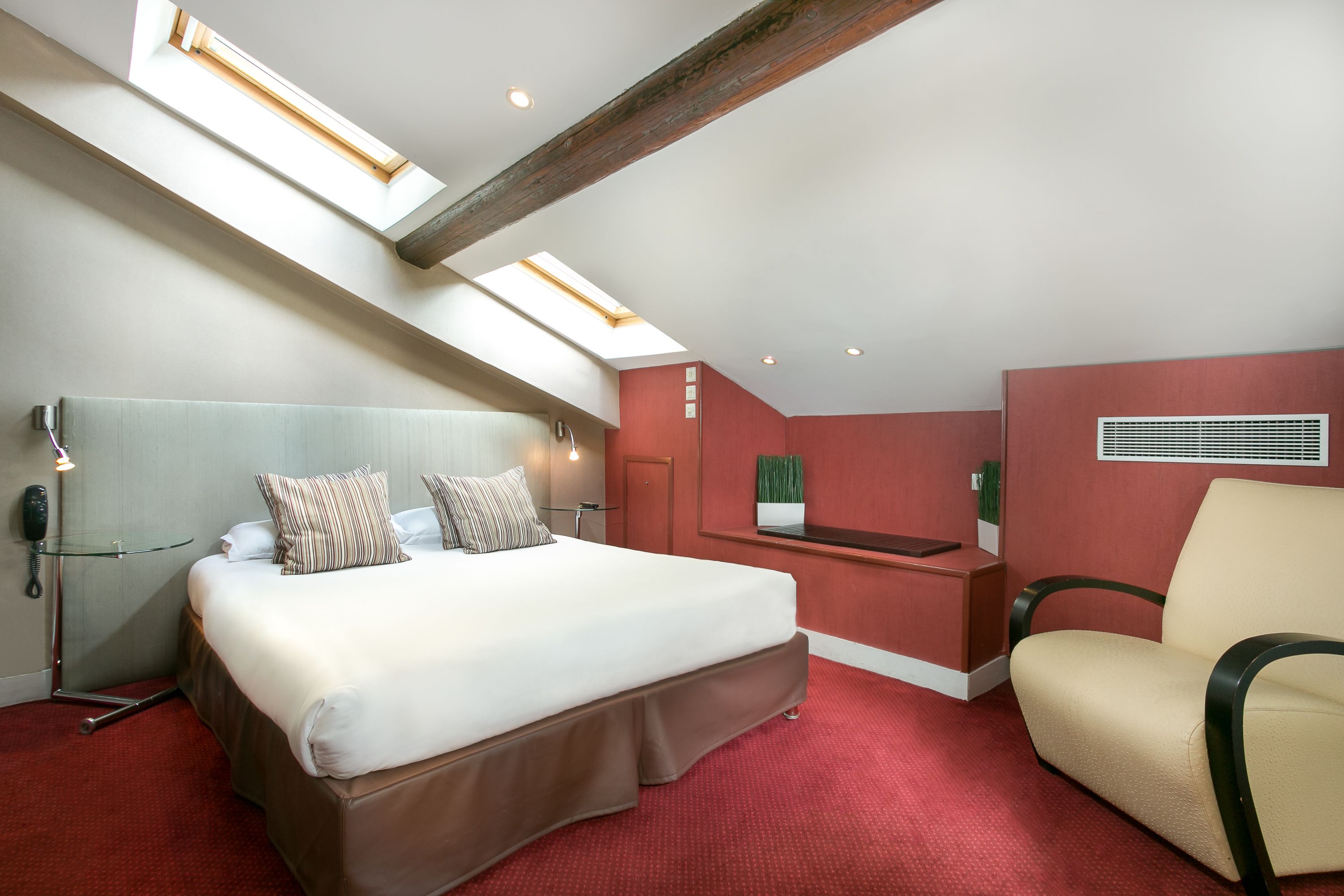 Une chambre d’hôtel avec un lit, un bureau, une chaise et une lucarne.