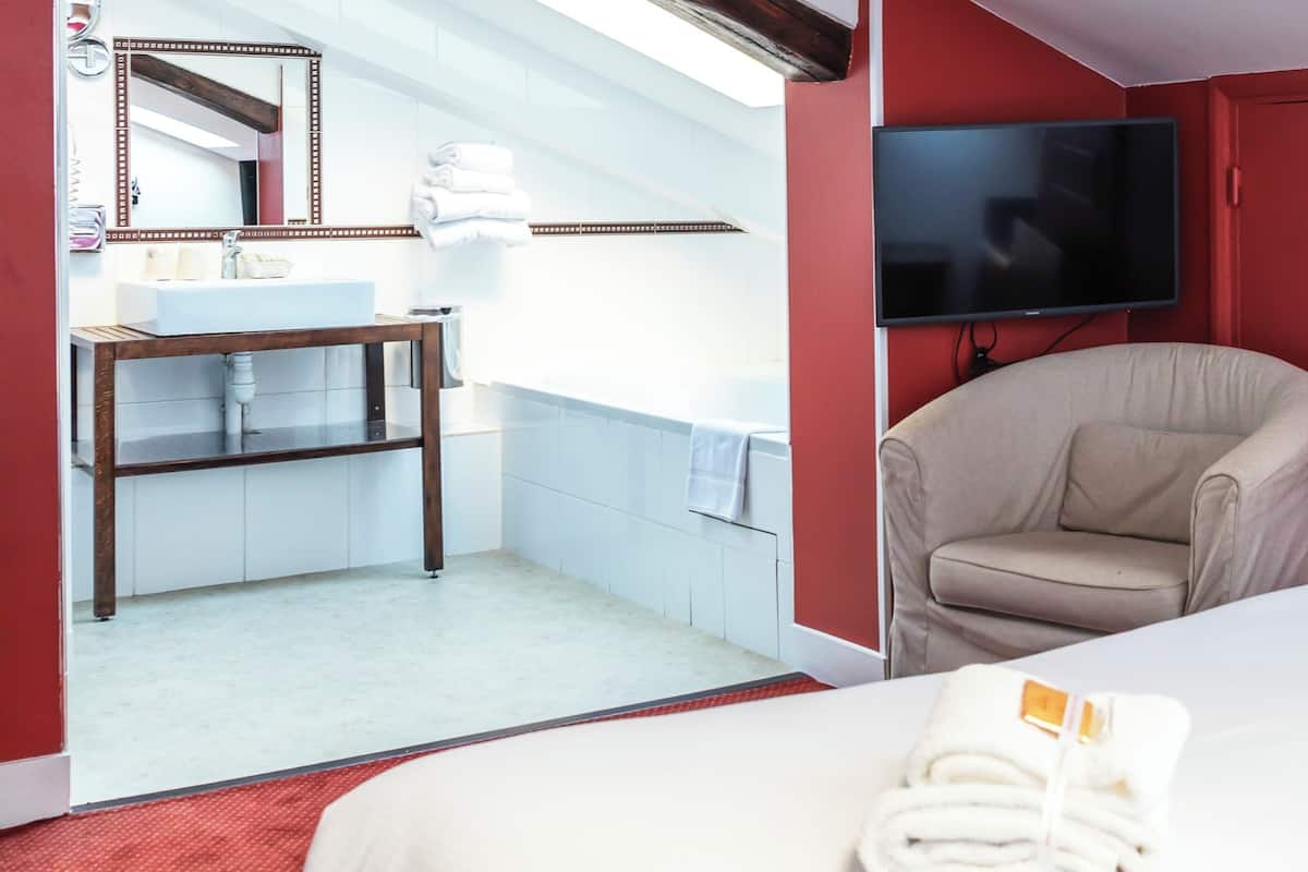 A hotel room with a bed, a TV, a chair, a bathroom with a sink and mirror, and towels on the floor.