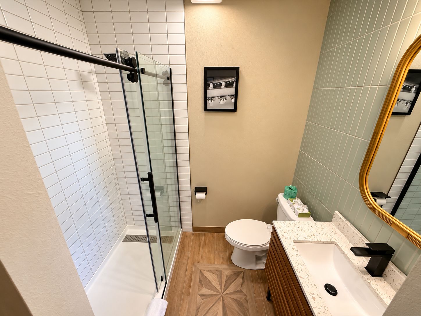 A bathroom with a glass shower enclosure, a toilet, a sink with a mirror, and a patterned floor.