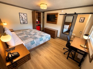 A hotel room with a bed, bedside table, desk, chair, and a large mirror.