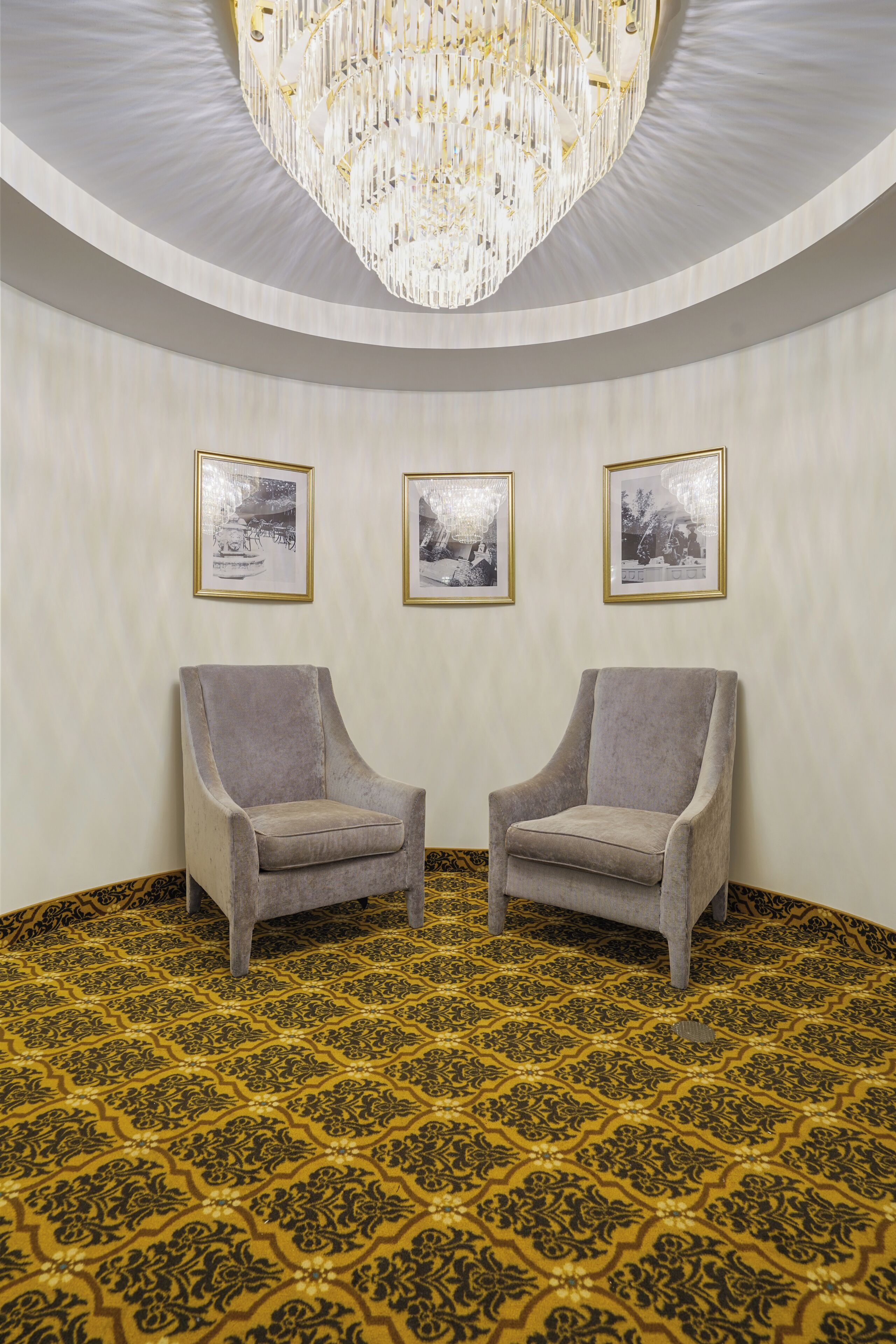 A room with a patterned carpet, two armchairs, and three framed pictures on the wall.