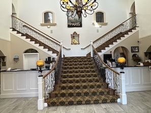 A grand staircase with ornate railings and patterned carpet leading to a landing. - Chateau Avalon Hotel & Spa (Kansas City)