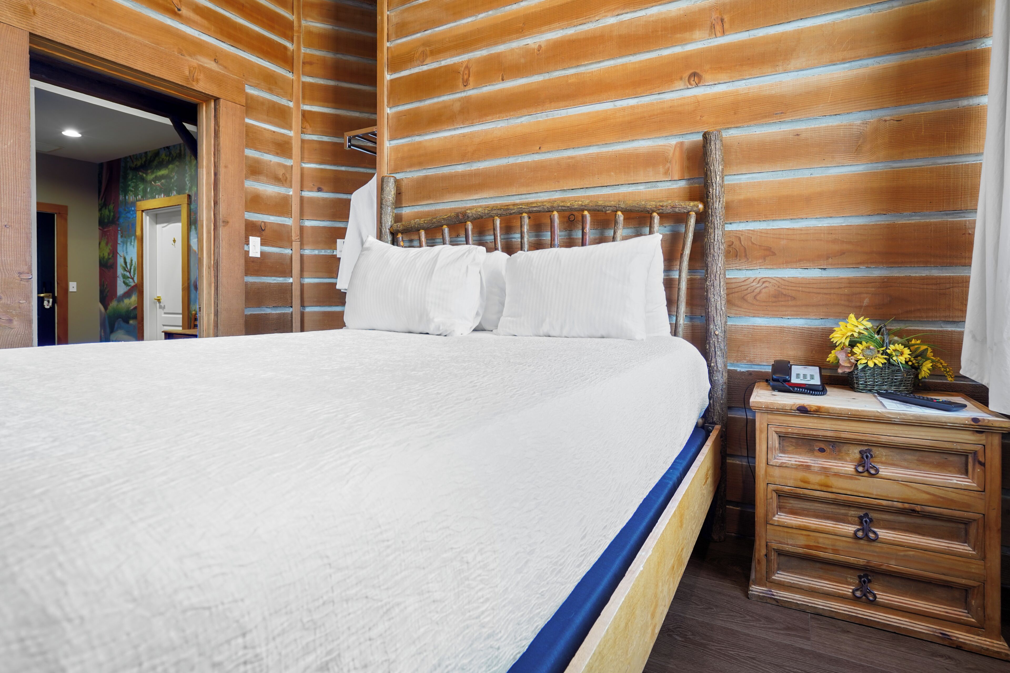 A hotel room with a large bed, wooden headboard, a nightstand with a phone and remote control, and a wall with horizontal wooden planks.