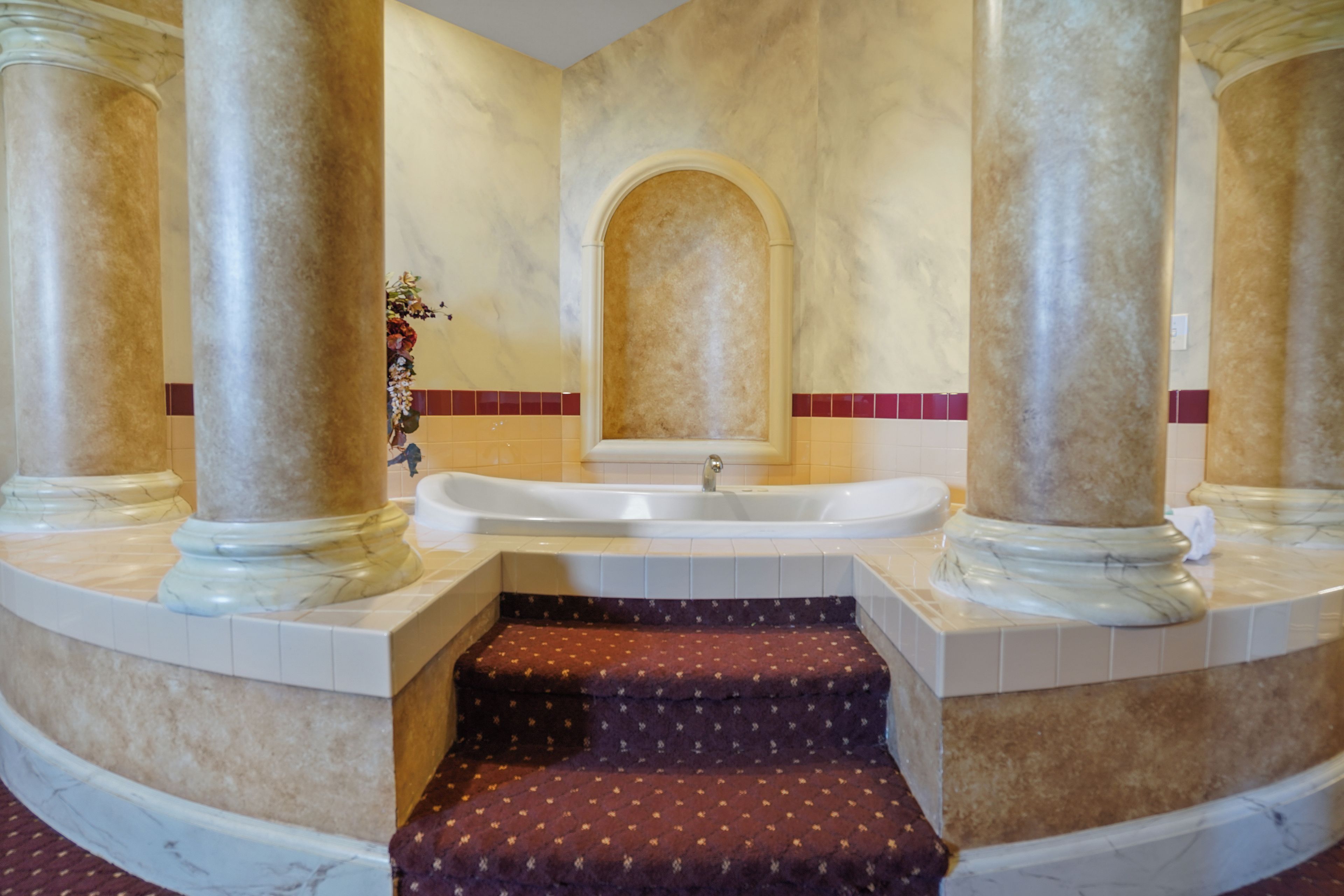 A bathroom with a marble floor, a bathtub, and a marble column.