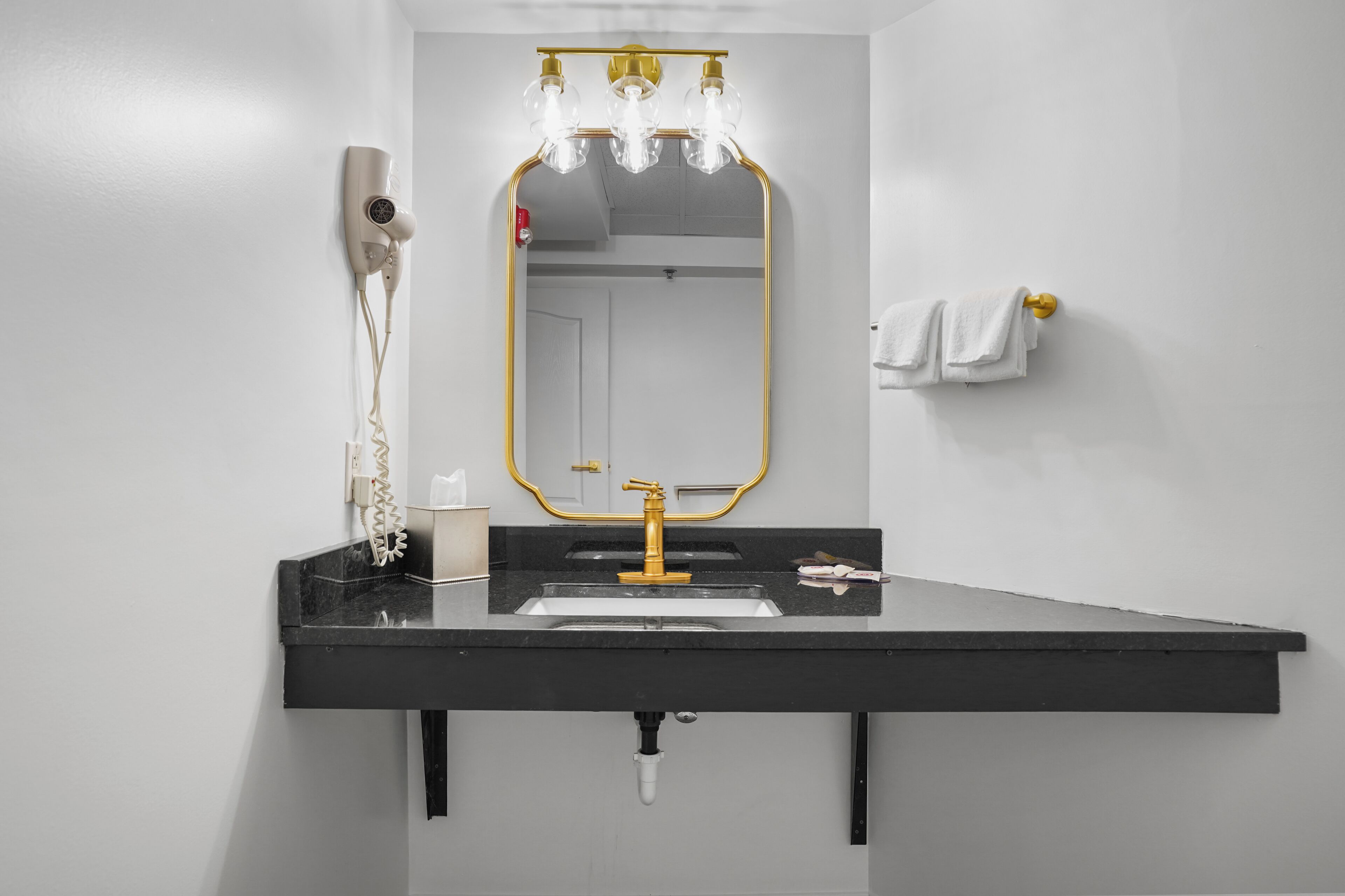 Ein Badezimmer mit schwarzem Waschtisch, goldenen Armaturen und einem Spiegel mit goldener Rahmung.