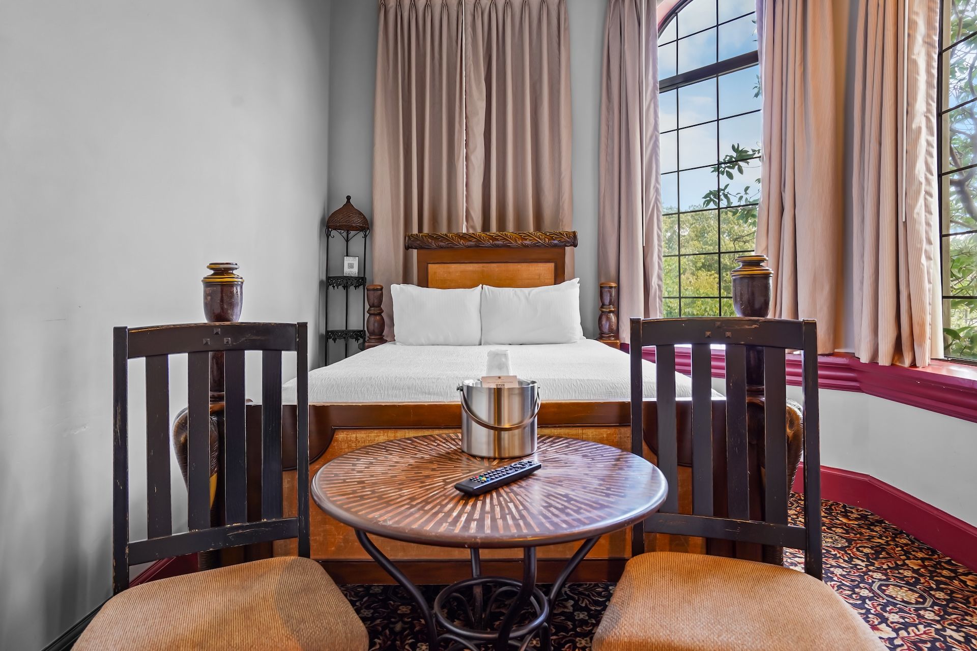 A hotel room with a bed, two chairs, a small table, and a window with curtains.