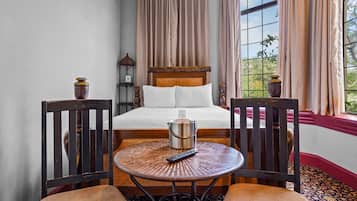 A hotel room with a bed, two chairs, a small table, and a window with curtains.