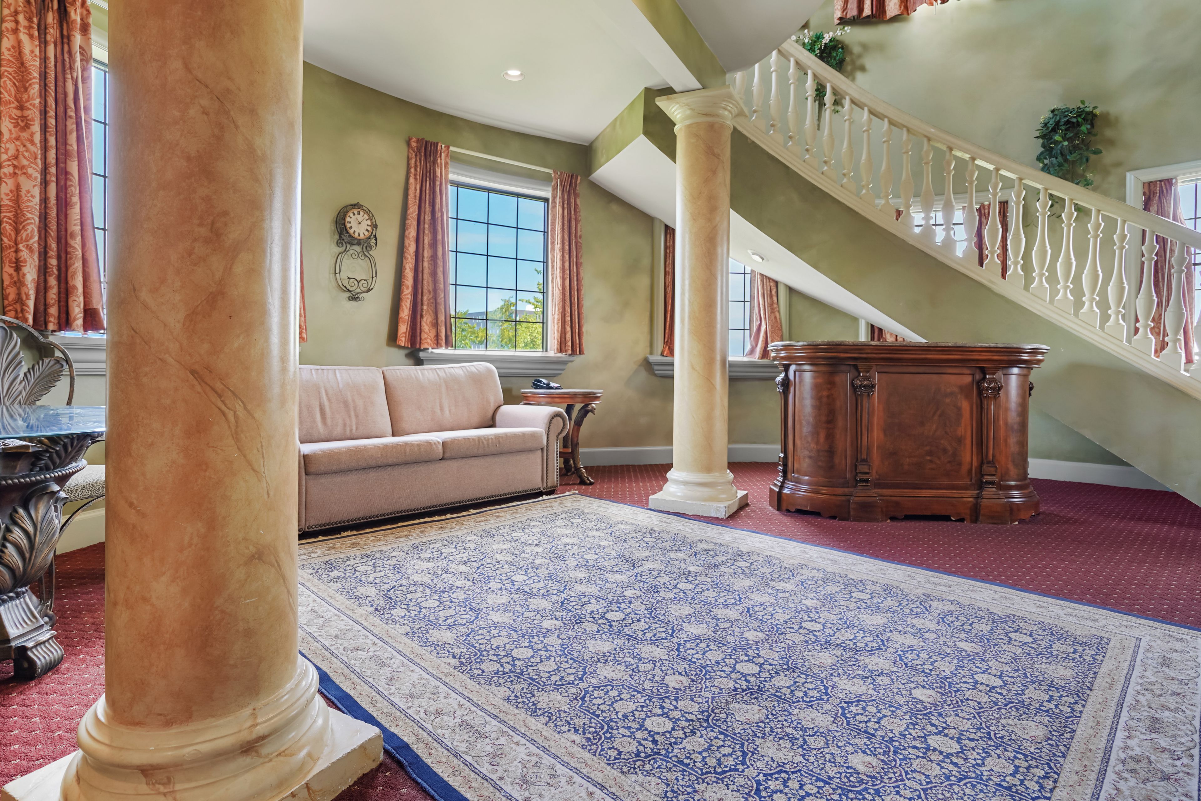 A spacious living area with a large window, a sofa, a wooden coffee table, and a staircase with a balustrade.