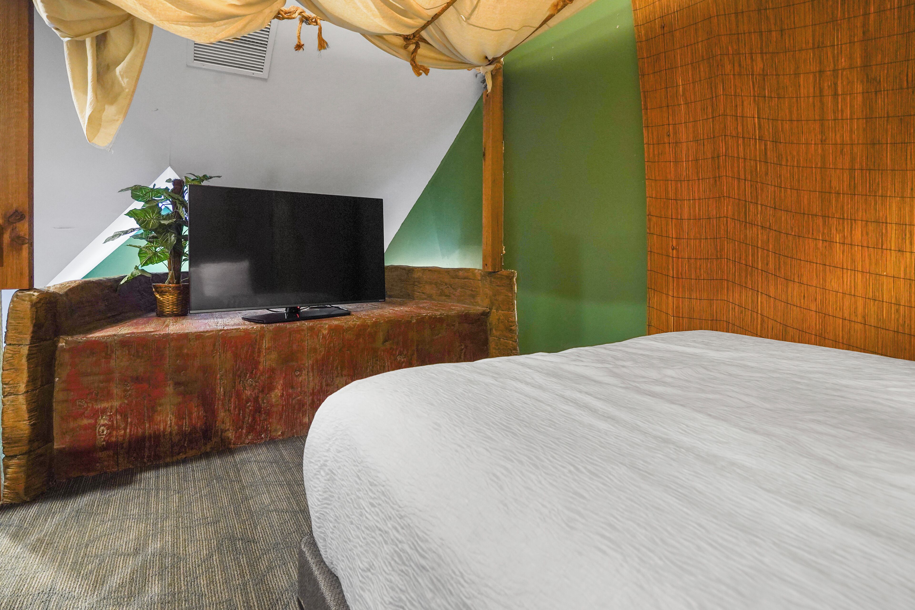 A room with a bed, a television on a wooden bench, and a green wall.