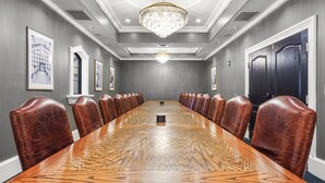 A conference room with a long wooden table, leather chairs, a chandelier, and framed pictures on the walls. - Chateau Avalon Hotel & Spa (Kansas City)
