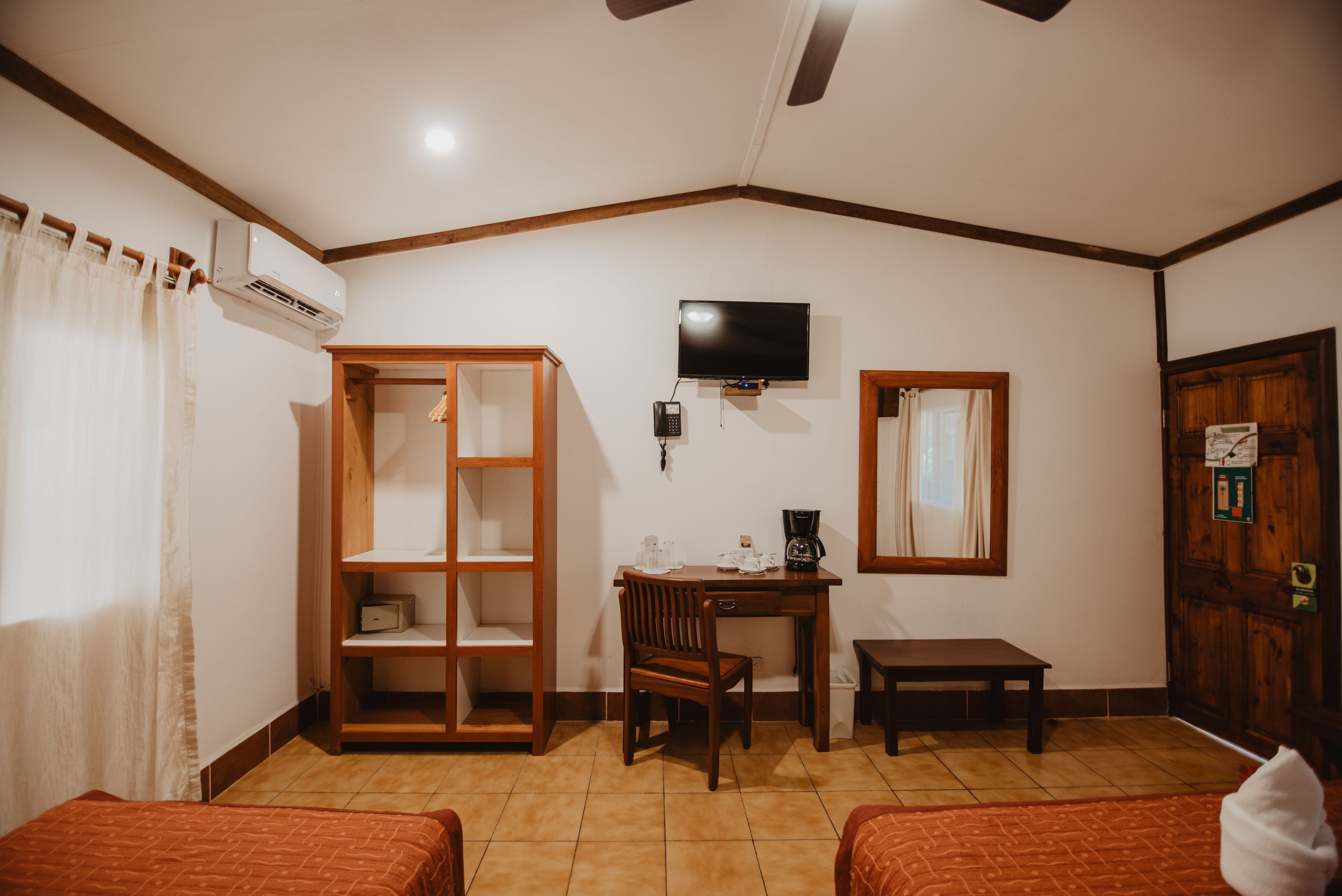 A room with two beds, a desk with a chair, a television, and an air conditioning unit.