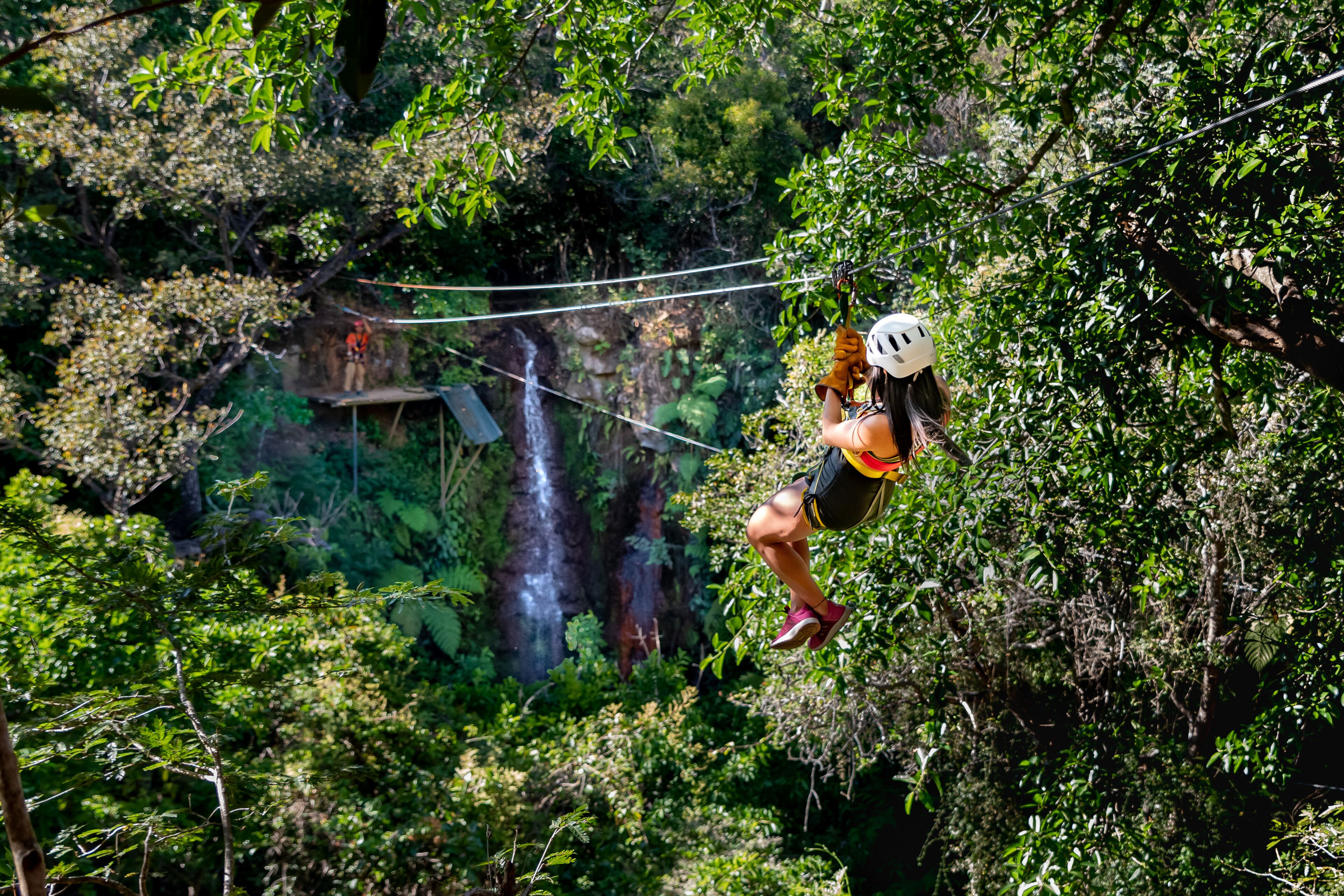Uma pessoa praticando tirolesa em meio à floresta, com uma cachoeira ao fundo.