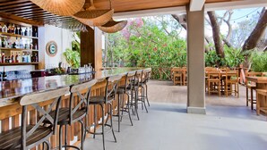 Un espace bar doté d’un comptoir en bois, de plusieurs tabourets et de lampes suspendues en osier.