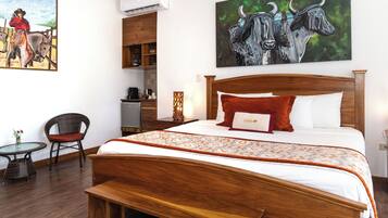 A hotel room with a large bed, a wooden headboard, a small table with a chair, and a painting of bulls on the wall.