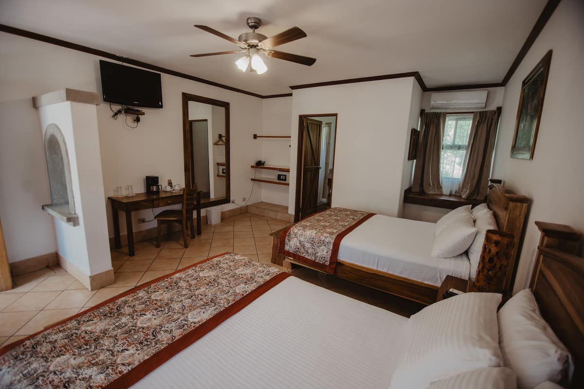 A hotel room with two beds, a desk, a television, and a ceiling fan.
