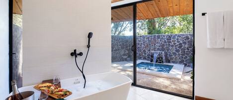Un baño moderno con una bañera independiente, una botella de vino y una bandeja de comida.