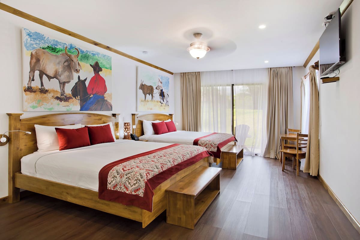 A hotel room with two beds, wooden headboards, a TV, a desk, and a chair.