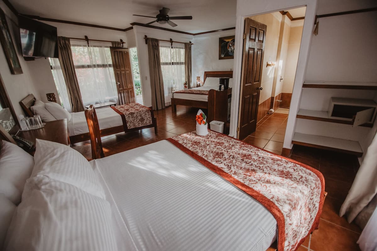 A hotel room with a large bed, a desk, a chair, a TV, and a ceiling fan.