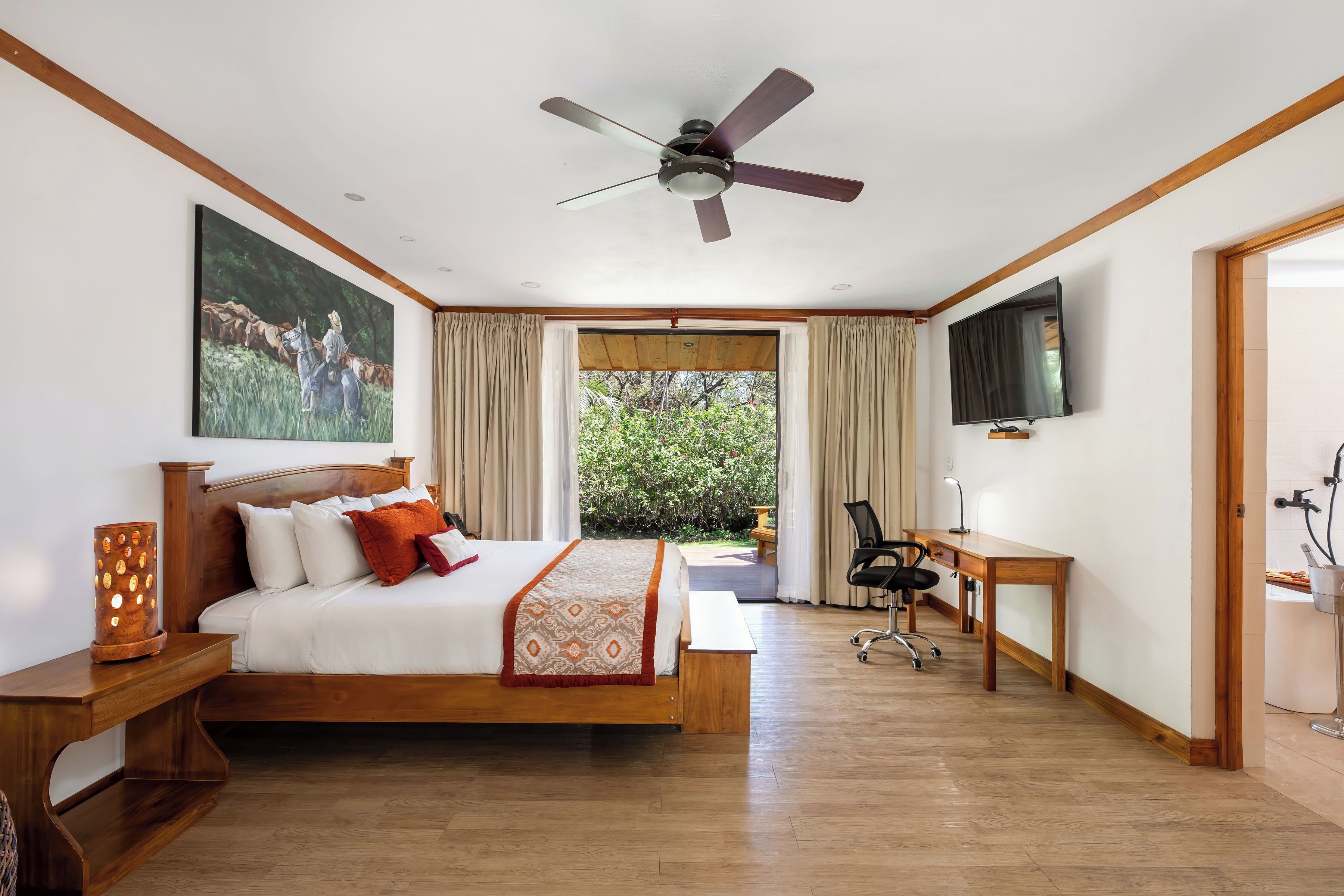 Un dormitorio amplio con una cama grande, ventilador de techo, televisor y escritorio con silla.