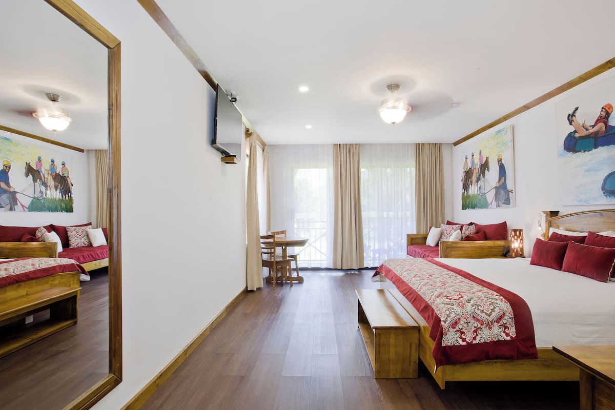 A hotel room with two beds, a wooden bench, a dining table, and chairs.