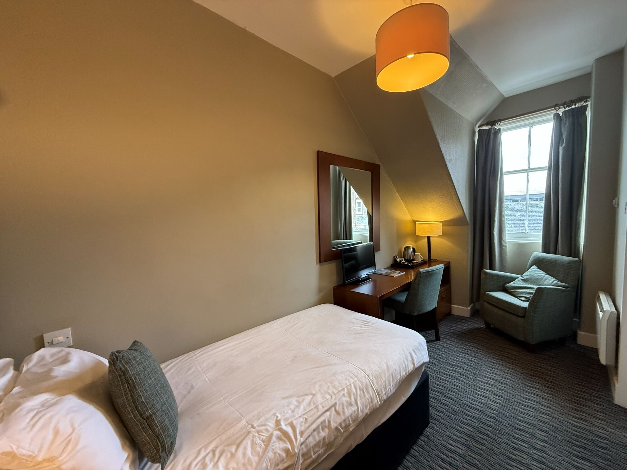 A hotel room with a single bed, a desk, a chair, a television, and a window with curtains.