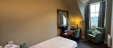 A hotel room with a single bed, a desk, a chair, a television, and a window with curtains.