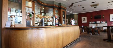 A bar area with wooden counter, shelves of liquor bottles, and a television mounted on the wall.