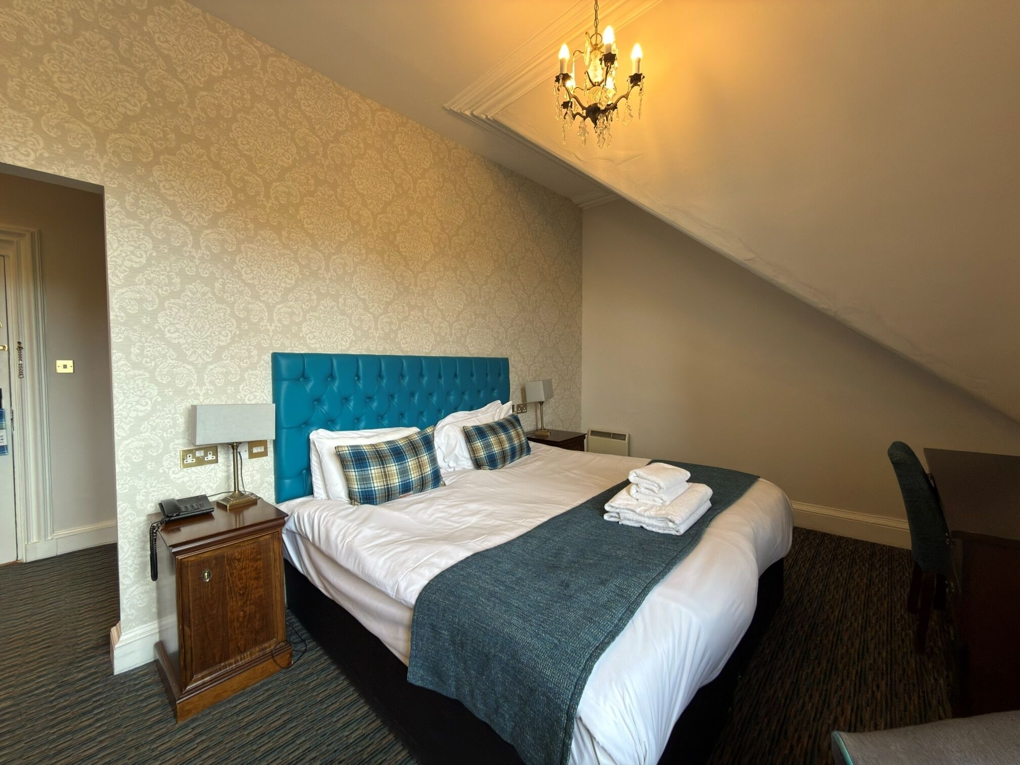 A hotel room with a large bed, a bedside table with a lamp, a telephone, and a chair.