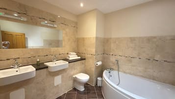 A bathroom with a bathtub, two sinks, a toilet, and a mirror.