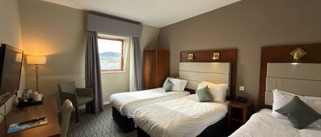 A hotel room with two beds, a desk, a chair, a lamp, and a window with curtains.