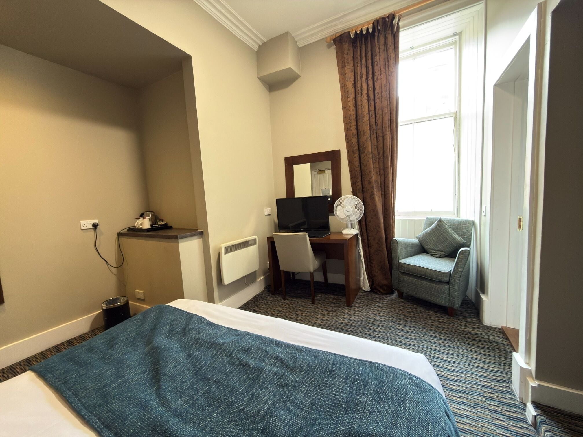 A hotel room with a bed, a desk, a chair, a television, a mirror, and a window with curtains.