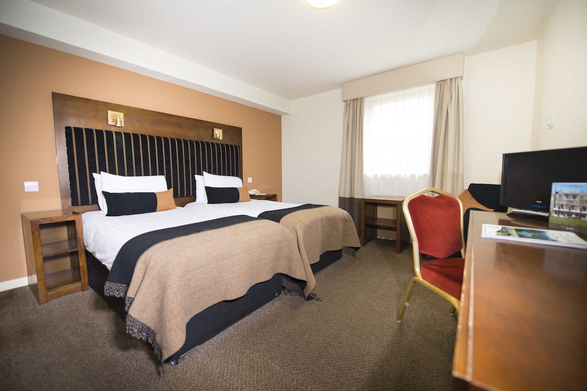 A hotel room with two beds, a desk, a chair, a television, and a window with curtains.