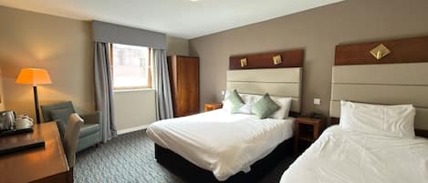 A hotel room with two beds, a desk, a lamp, and a window with curtains.