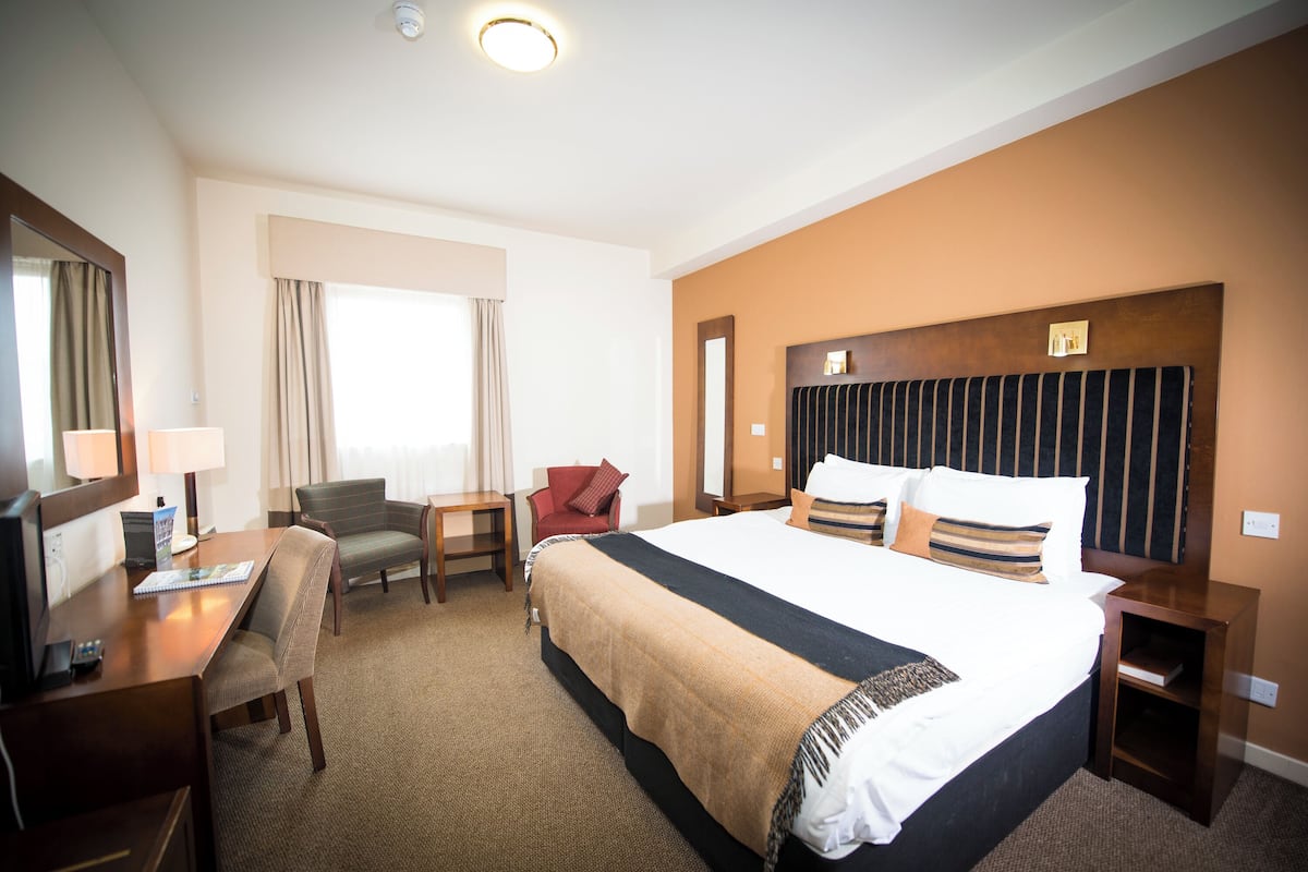 A hotel room with a large bed, a desk, a chair, and a small table.