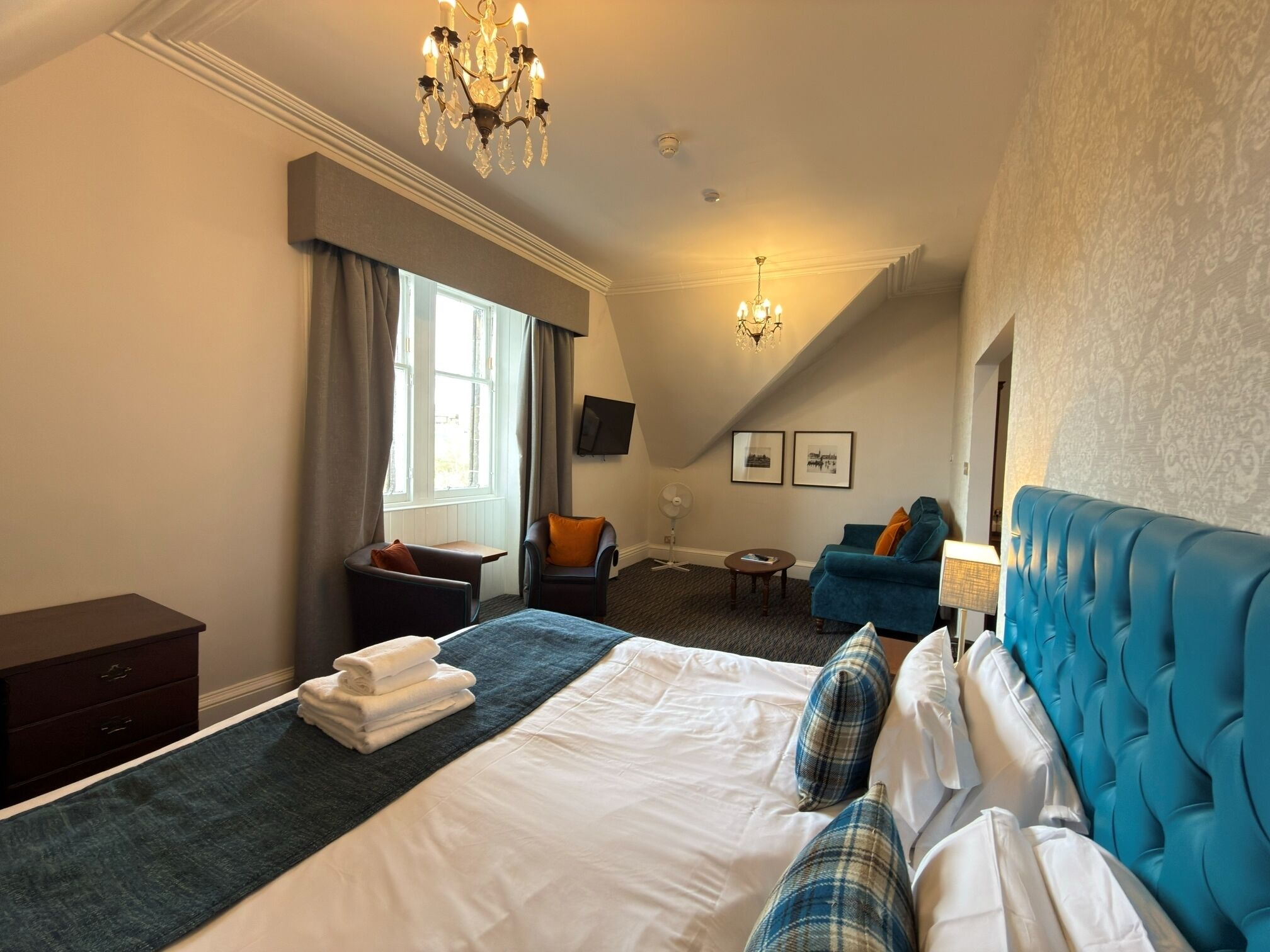 Een hotelkamer met een groot bed, een zithoek met een blauwe bank, een televisie en een kroonluchter.